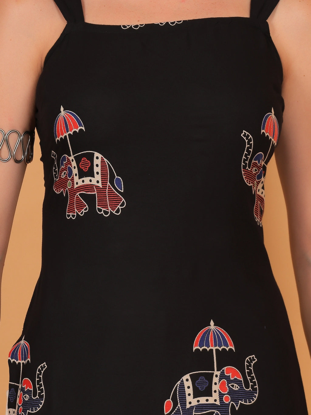 Black sleeveless short kurti with an elephant print paired with light beige pants and silver jewelry.