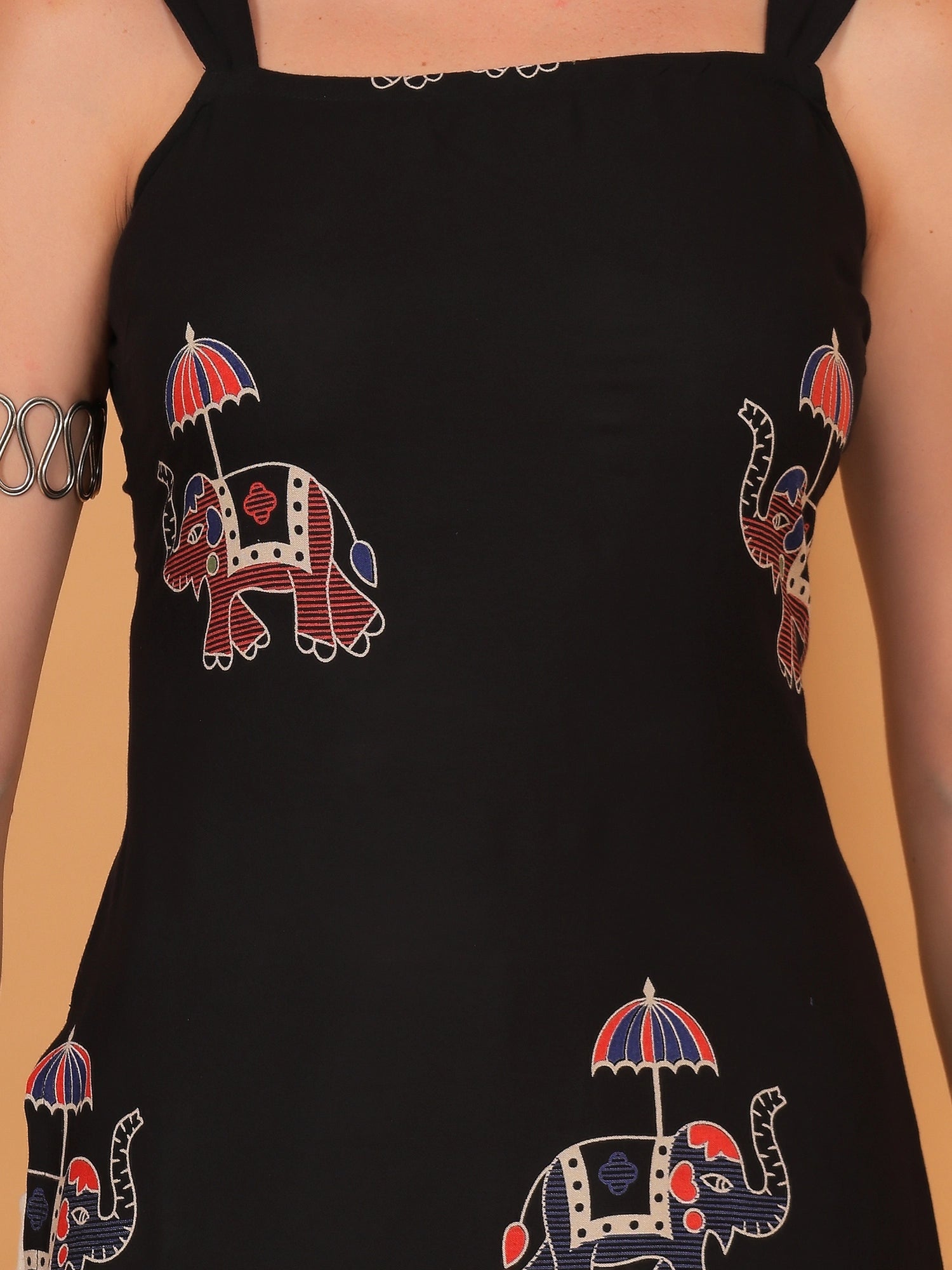 Black sleeveless short kurti with an elephant print paired with light beige pants and silver jewelry.