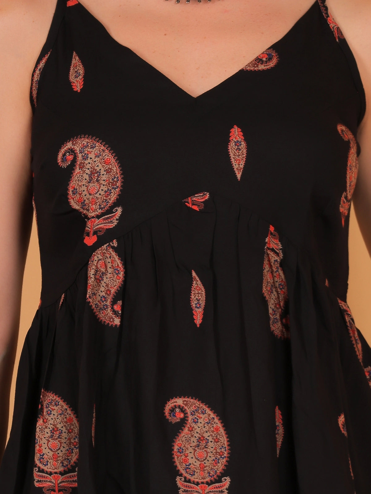 Front close-up shot of the Indira black sleeveless ethnic top, showcasing the detailed golden motif print on opaque rayon fabric against a solid peach background.
