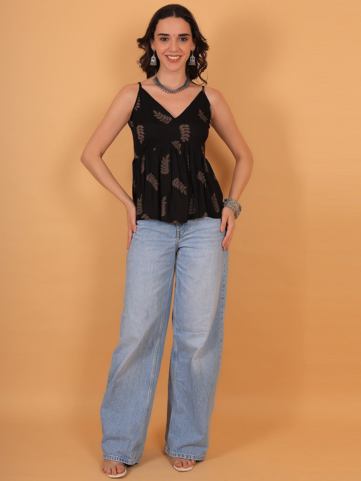 Mid-length lifestyle shot of a modern black sleeveless kurti top with a leaf pattern paired with denim jeans, ideal for a casual daily wear look.