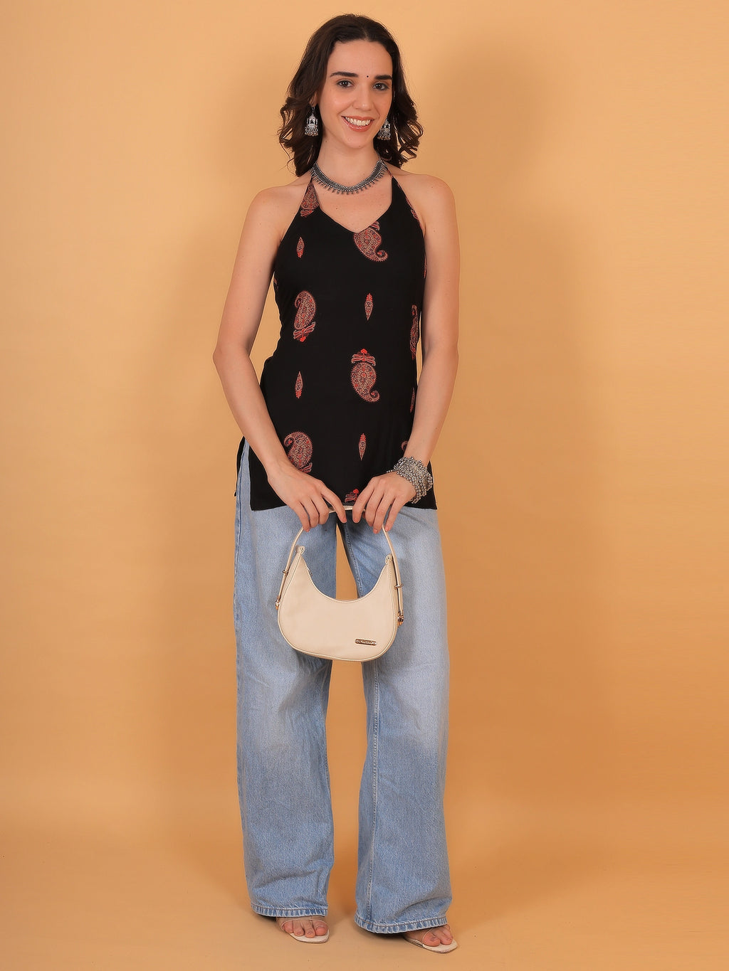 Full-length lifestyle shot of a modern black sleeveless kurti with red floral paisley details paired with denim jeans for a trendy college or casual ethnic look.