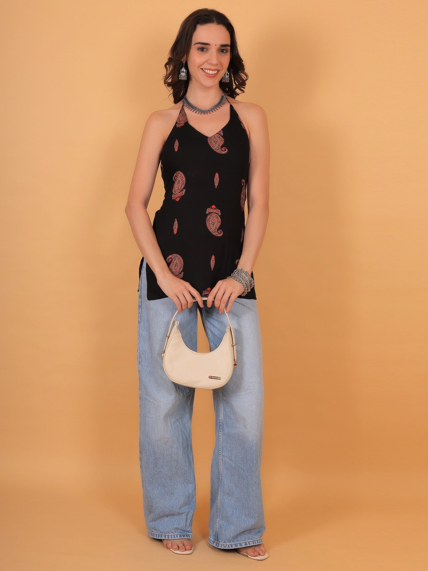 Full-length lifestyle shot of a modern black sleeveless kurti with red floral paisley details paired with denim jeans for a trendy college or casual ethnic look.