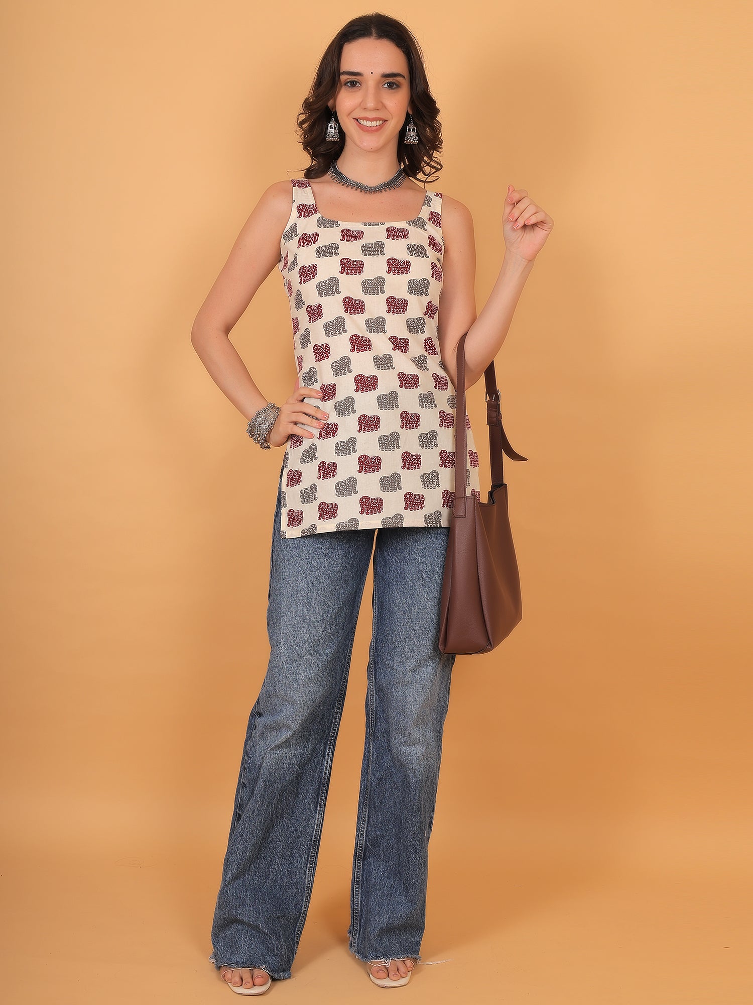 Woman wearing straight cut cream ethnic top paired with blue jeans and brown tote bag.