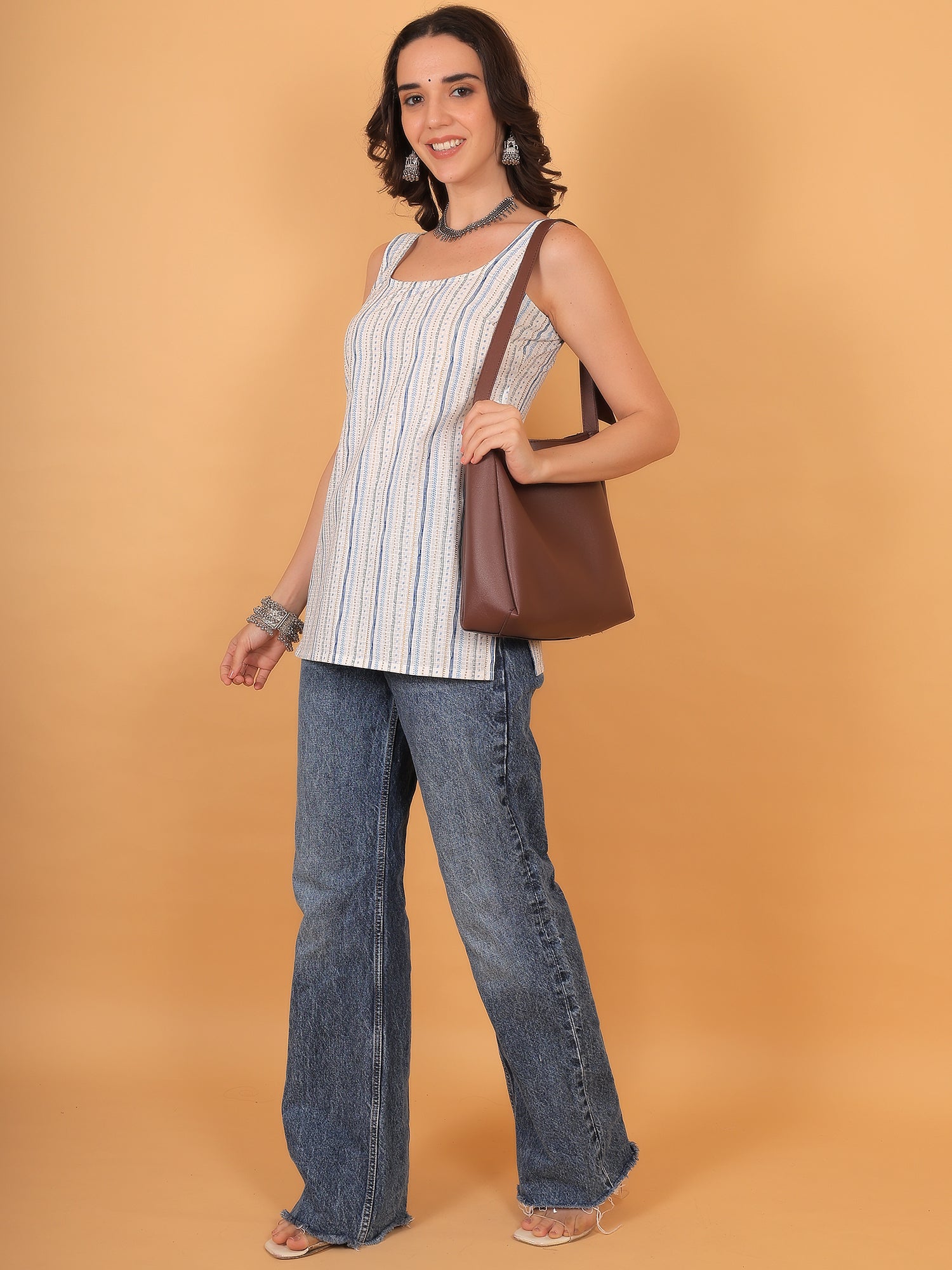 Woman wearing straight cut white ethnic top paired with wide-leg blue jeans and brown tote bag.
